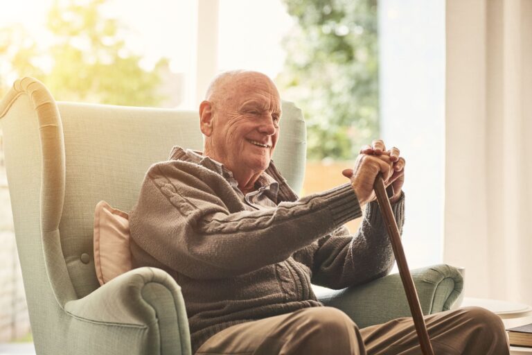 Man sitting in a chair with a cane, the sun is shinning behind him