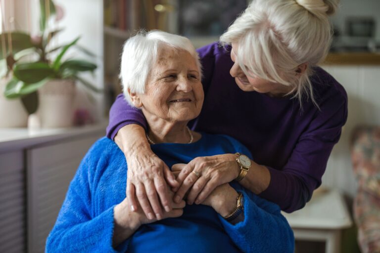 Woman hugging her grandmother from behind, both smiling